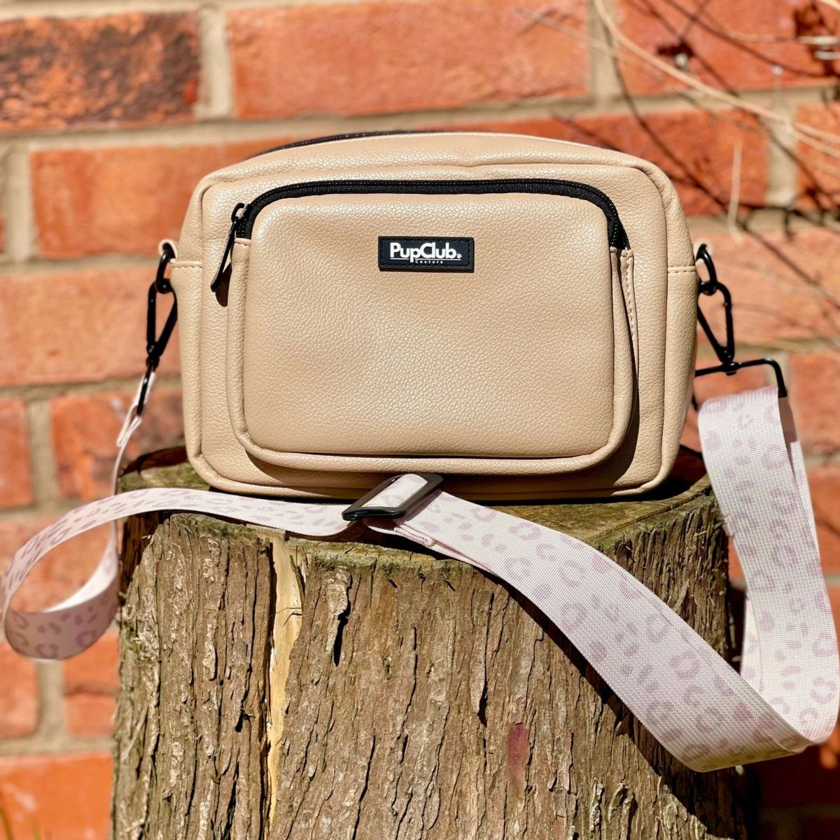 Tan crossbody bag with front zipper pocket, PupClub logo, and patterned wrist strap