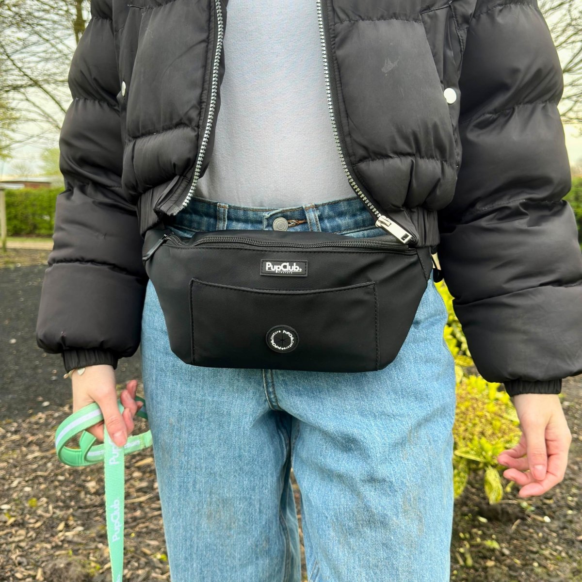 Black bum bag with front zip and circular logo patch, worn on waist