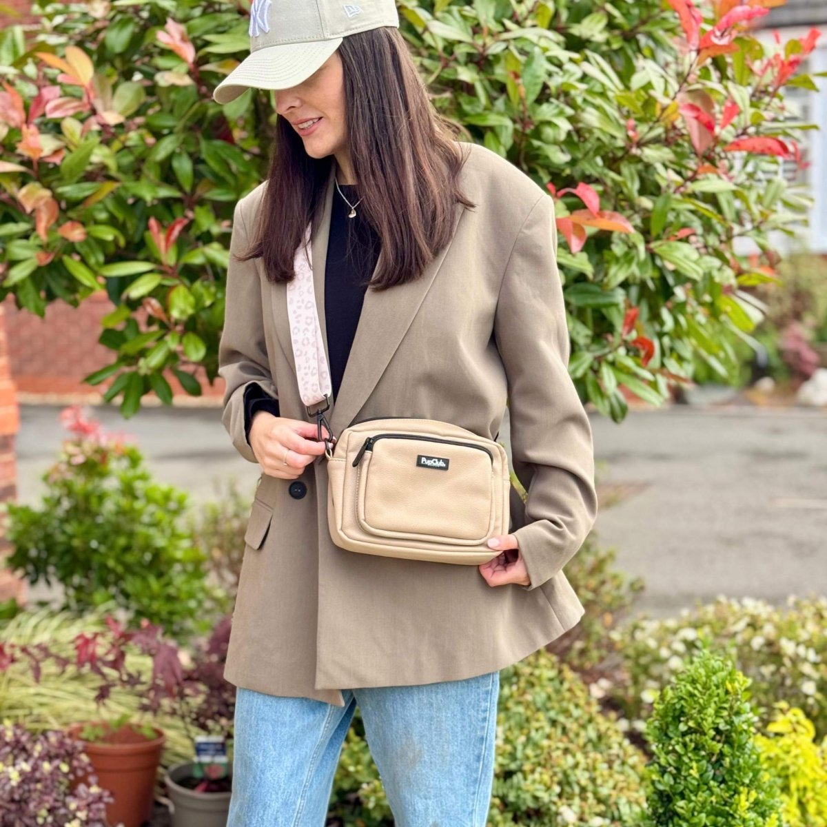 Tan crossbody dog walking bag on a person wearing a coat; front zip pocket visible
