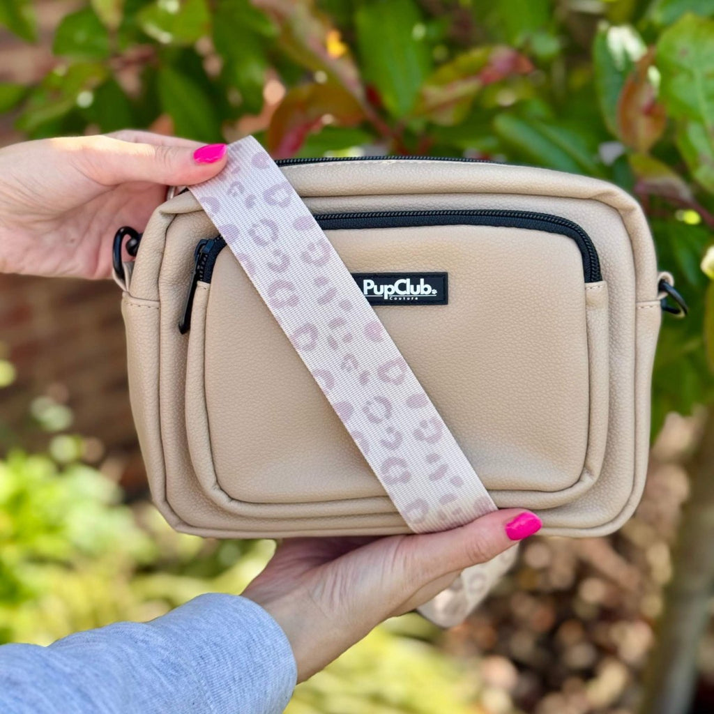 Tan crossbody bag showing front pocket and patterned strap, held in hands outdoors