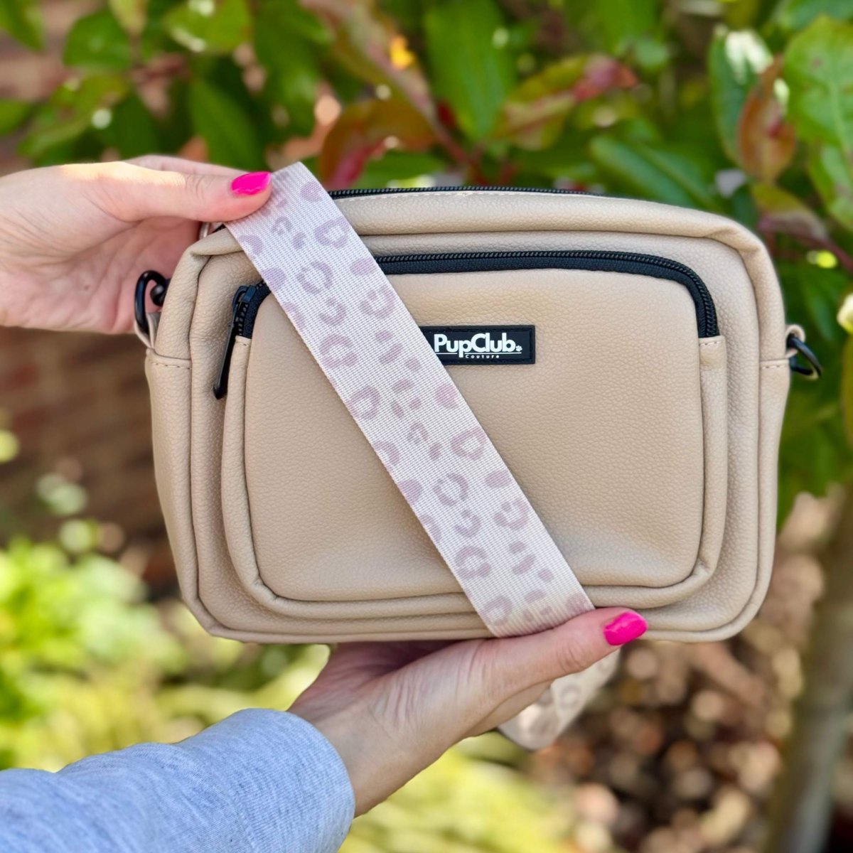 Tan crossbody bag showing front pocket and patterned strap, held in hands outdoors