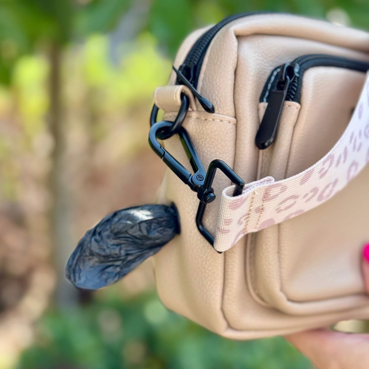 Tan crossbody bag detail with black D-ring clips and patterned leash strap