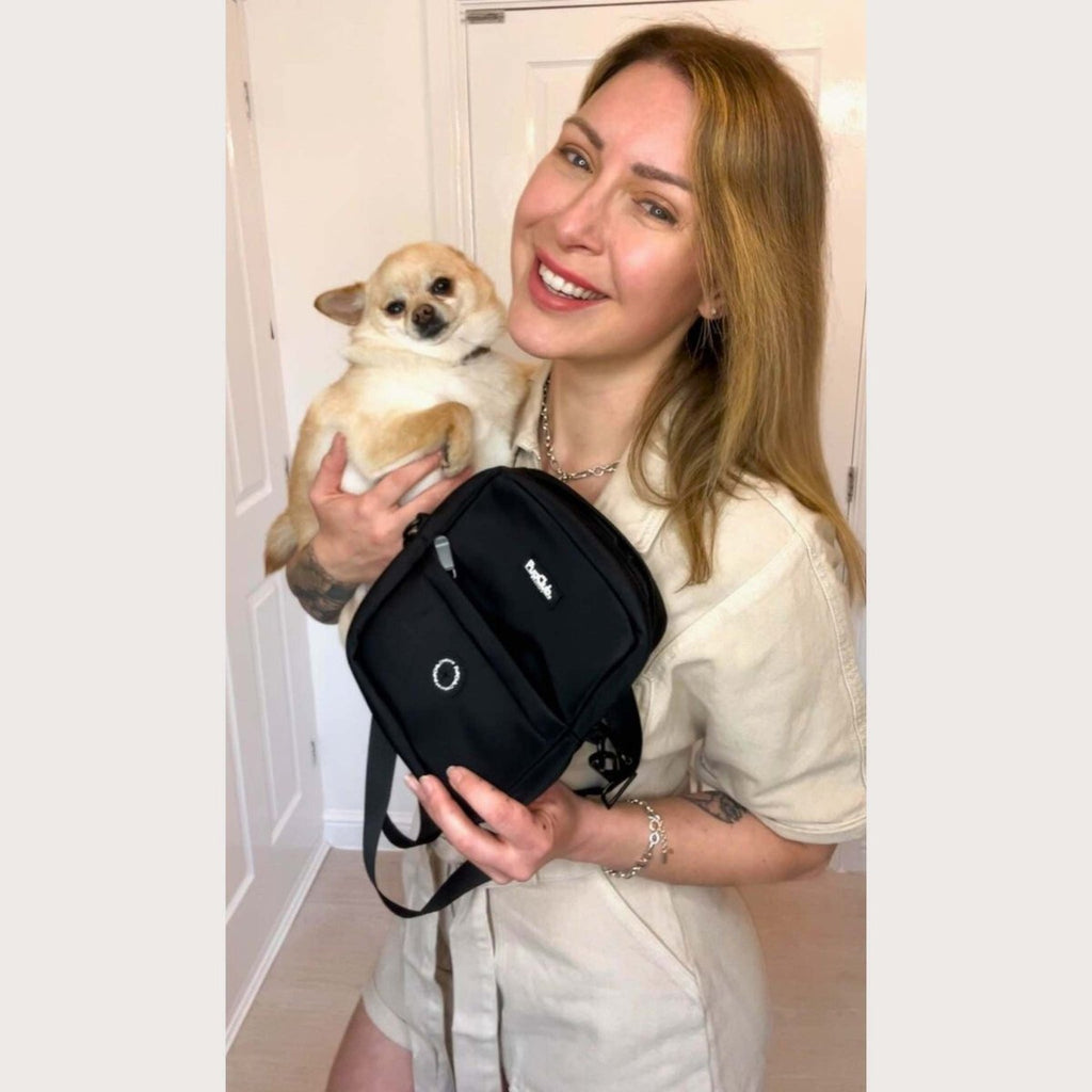 Black mini dog walking bag held by strap with front pocket and logo badge