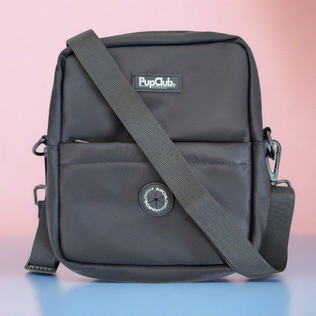 Mini dog walking bag in black with front pocket, logo patch, and adjustable shoulder strap