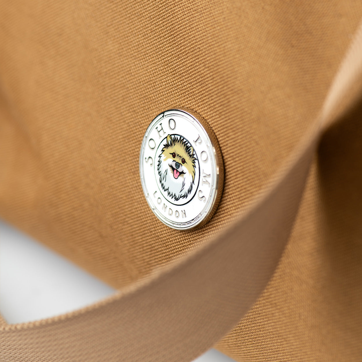 Brown canvas pet carrier with circular logo patch near front corner