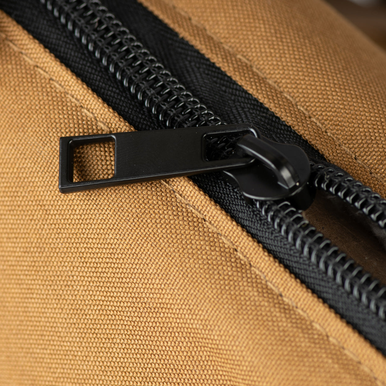 Pet carrier zipper pull with black strap and metal hardware on tan canvas