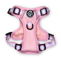 Pastel pink dog harness with black buckles and striped webbing at the straps