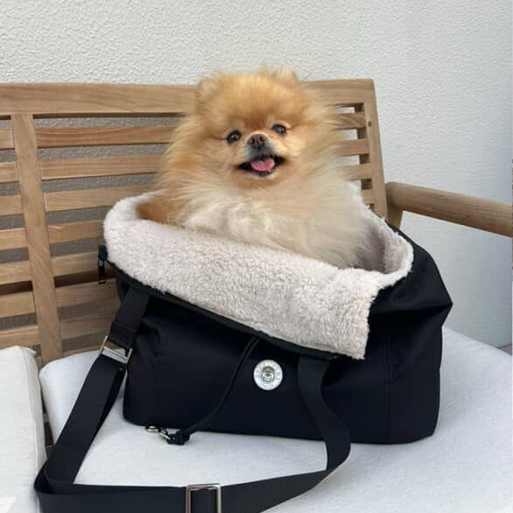 Pomeranian sitting in black pet carrier with cream fleece bedding and strap